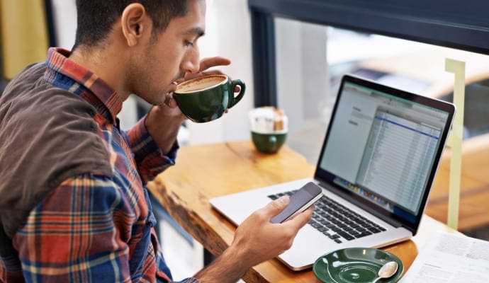 Mand drikker kaffe, mens han kigger på sin telefon.