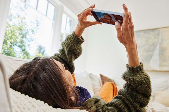 Kvinde ligger ned og kigger på en mobiltelefon